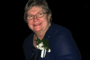 Dena in later years, smiling in a blue dress with a corsage
